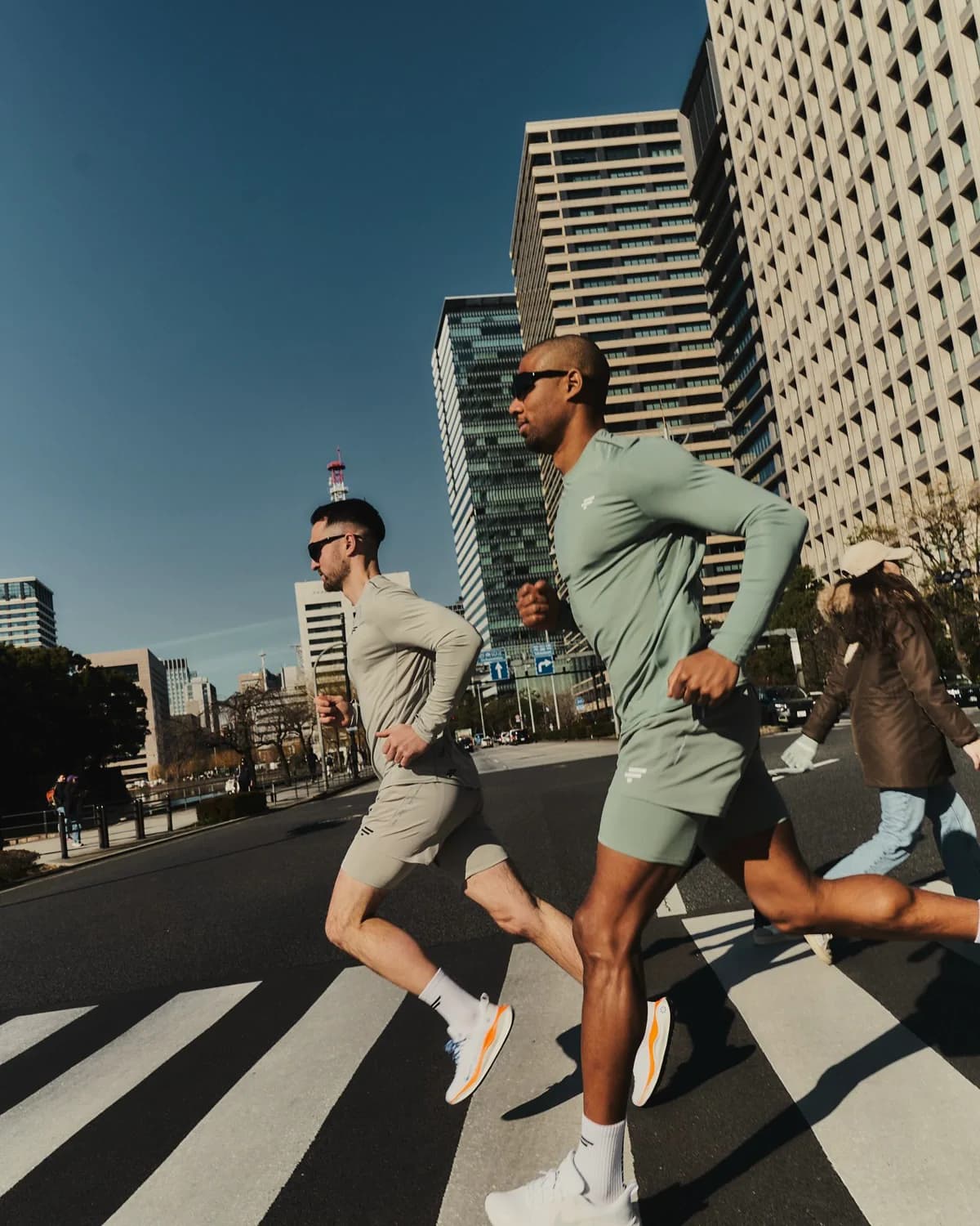 Corredores atravessam uma faixa de pedestres entre prédios, durante um treino de corrida urbana