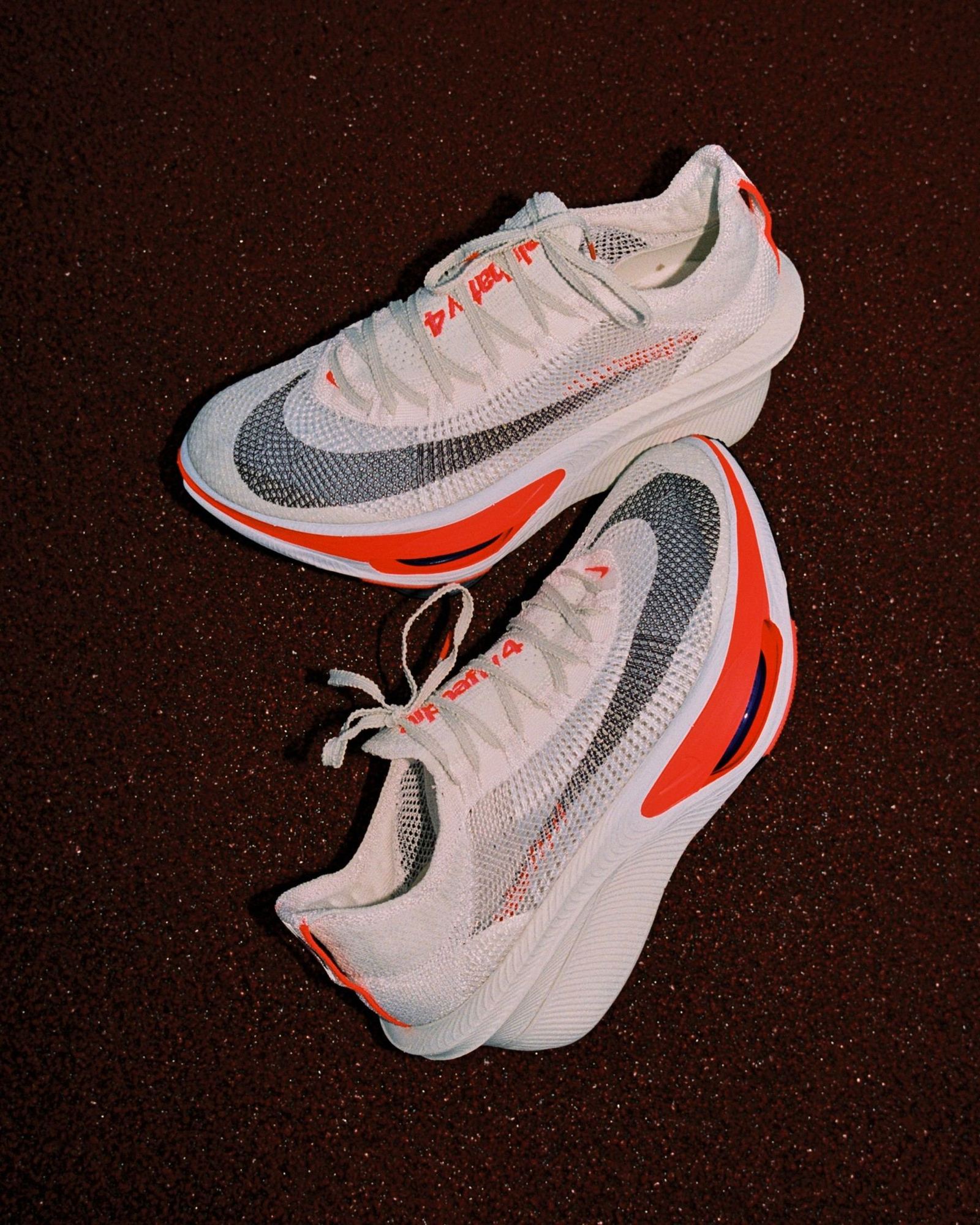 Par do Nike Alphafly 4 branco com detalhes em laranja sobre a pista de atletismo vermelha, com o Flyplate e a unidade Air Zoom visíveis na lateral