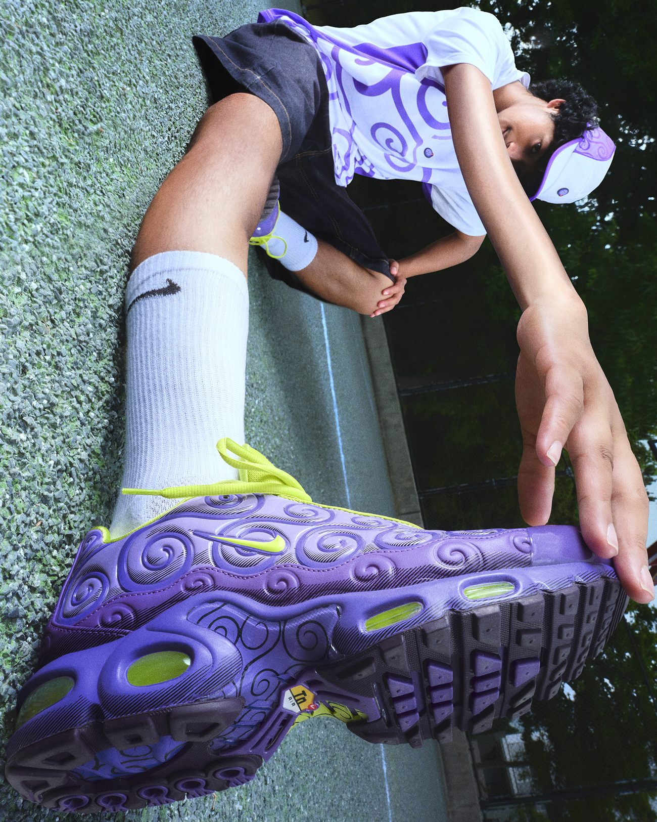 Detalhe do Air Max Plus roxo Gomu Gomu no pé de um garoto sentado em um muro, com as espirais em relevo na lateral