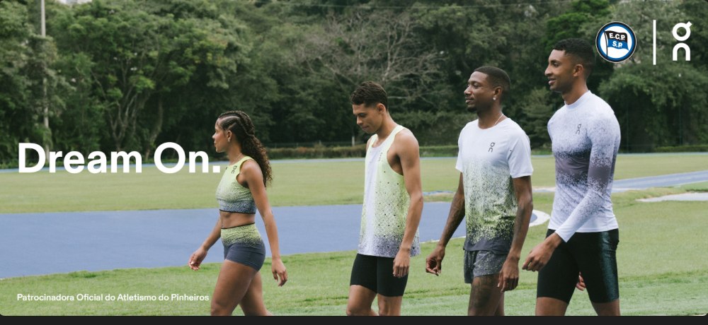 Atletas do Pinheiros em uniforme On caminhando na pista, com o letreiro Dream On