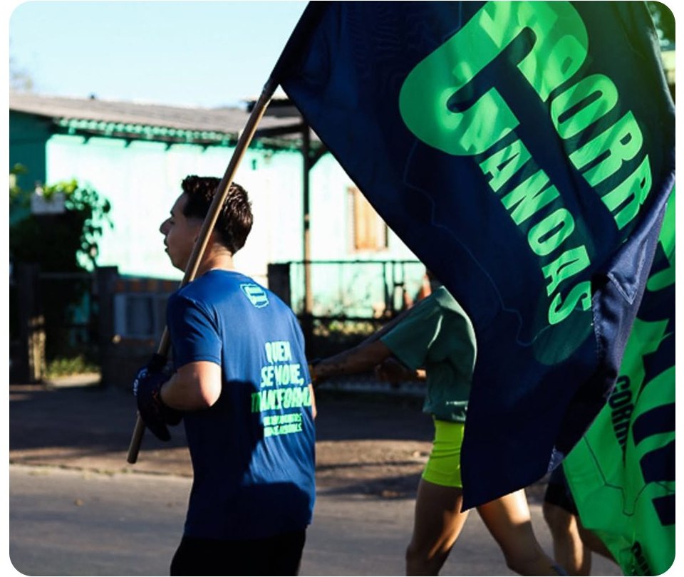 Corredores do Corre Canoas na rua com a bandeira azul e verde do clube ao vento