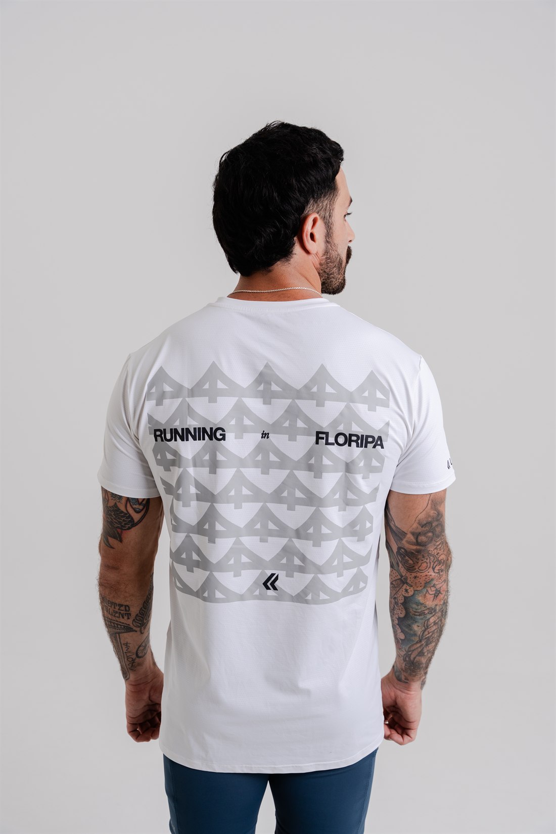 Costas de camiseta branca da coleção Running in Floripa, com padrão tonal em cinza claro e a frase RUNNING in FLORIPA